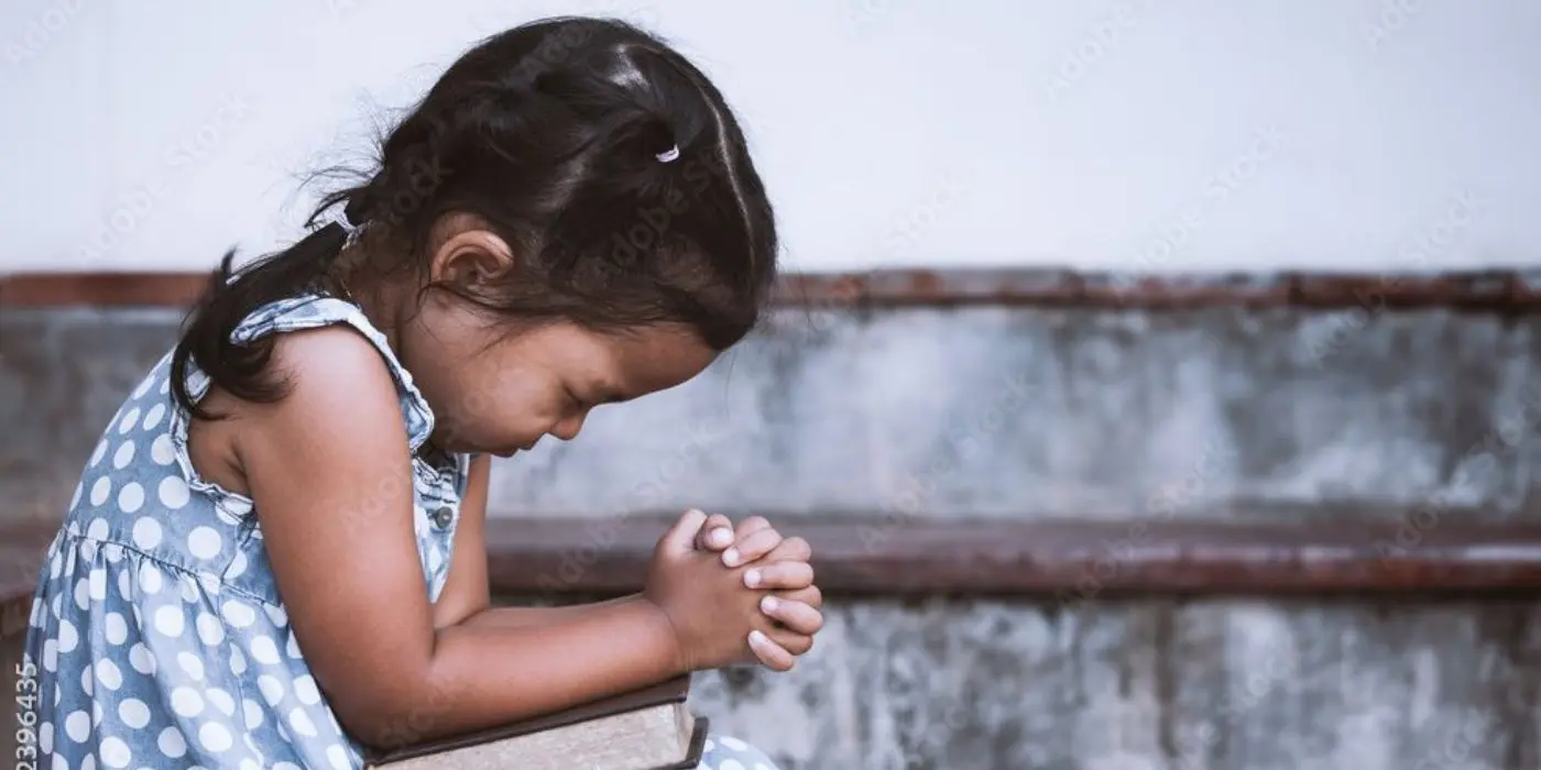 A little girl is praying with her hands in front of her face.