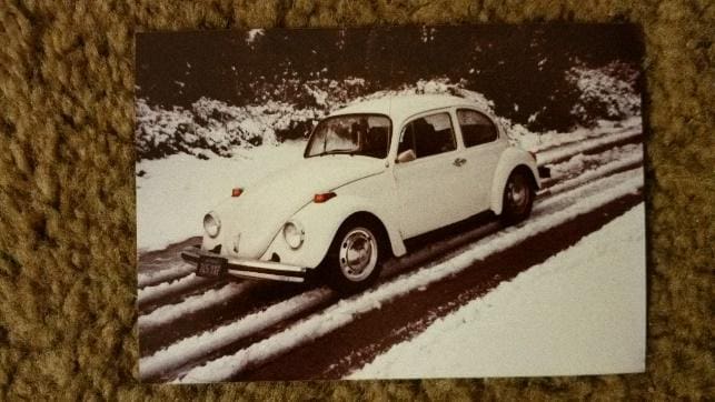 A white car is driving down the road in snow.