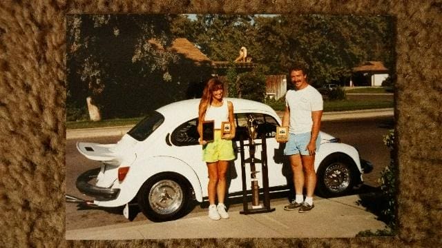 A man and woman standing next to a white car.